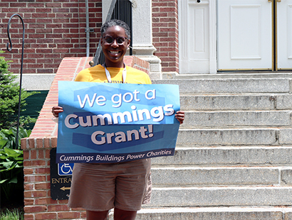 VP of Enrollment & Student Development Lorretta Holloway holding a sign in front of Dwight Hall that says "We received a Cummings grant!"
