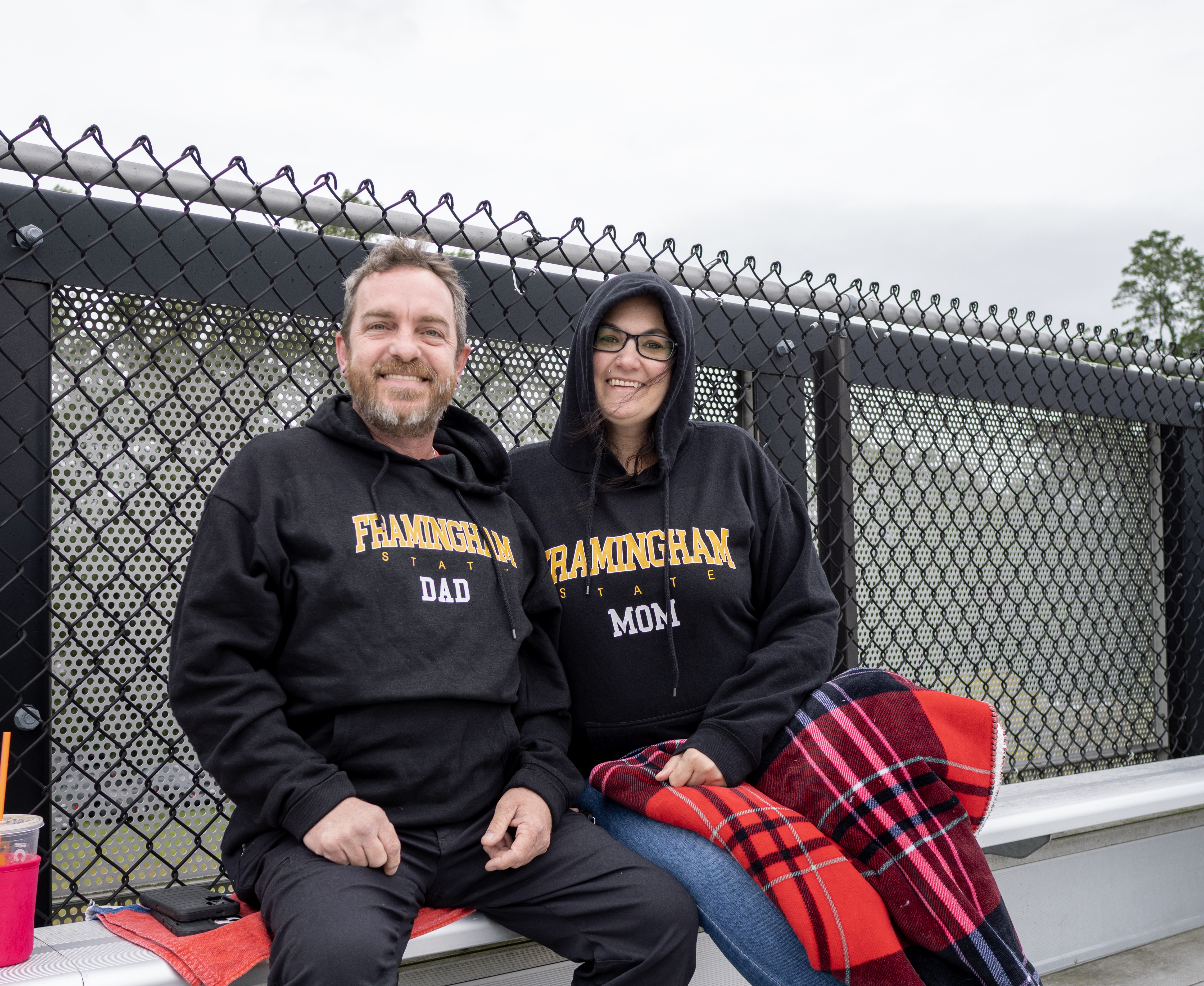 Two parents in matching 'Framingham State University Mom' and 'Framingham State University Dad' sweatshirts