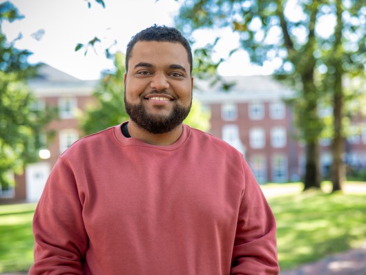 Photo of César standing in front of buildings at Framingham State University