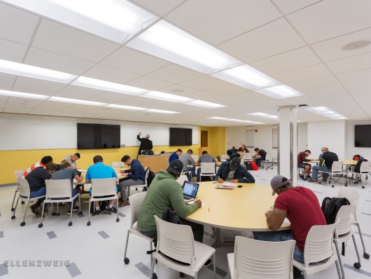 Students at round tables in a classroom with a professor teaching up at a white board