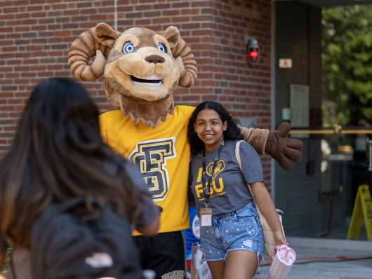 A student poses with Sam the Ram mascot