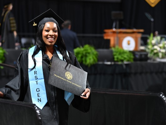 A student with a first-gen sash holds her Framingham State University diploma at commencement