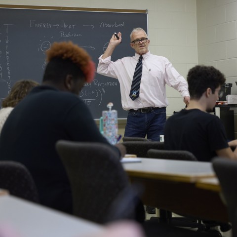 Teacher in Classroom pointing at chalkboard